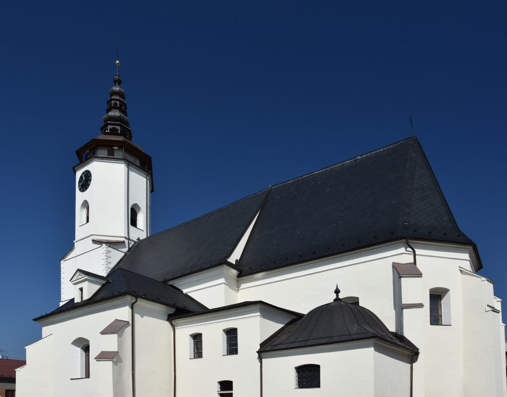Kostel svatého Mikuláše. Bílá fasáda ostře kontrastuje s modří podzimní oblohy.